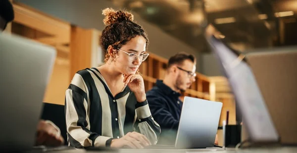 Retrato de uma jovem hispânica entusiasmada que trabalha no computador em um escritório moderno e brilhante. Agente de Recursos Humanos confiante sorrindo feliz enquanto colabora on-line com os colegas