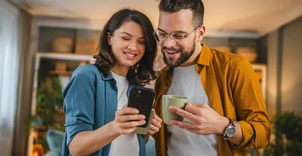 Casal adulto, homem e mulher, marido, esposa, tomar uma xícara de café, usar o celular, pesquisar na internet, rede social, sorriso feliz