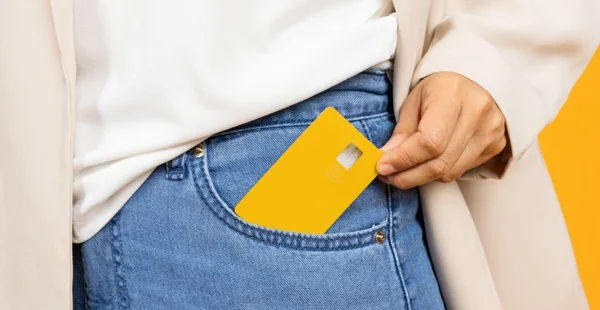 A Imagem mostra uma pessoa vestindo calça jeans colocando um cartão amarelo em um bolso. O fundo é amarelo e a pessoa esta usando uma camisa branca e um casaco pede