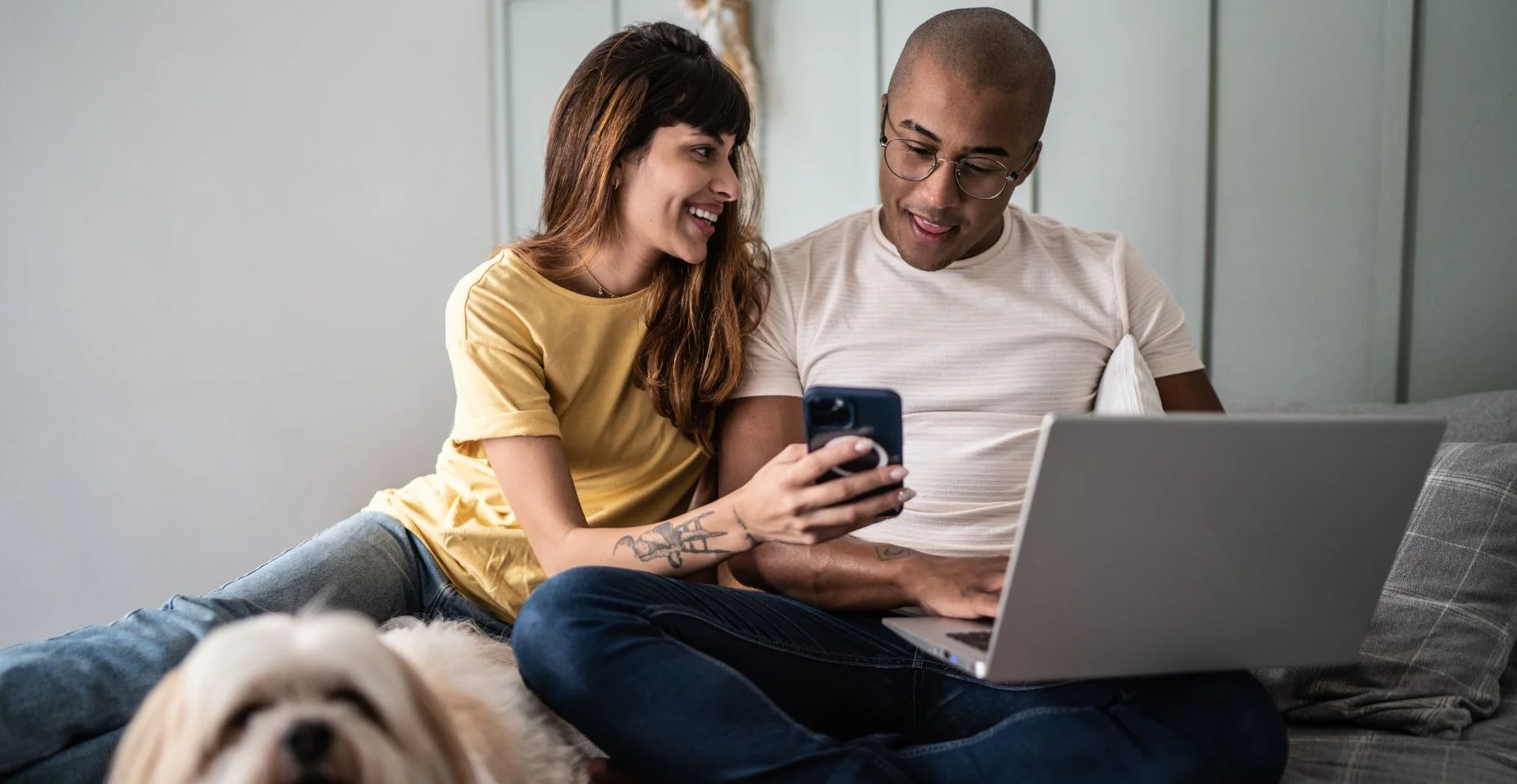 ovem mostra algo para marido no celular com o cachorro na cama em casa