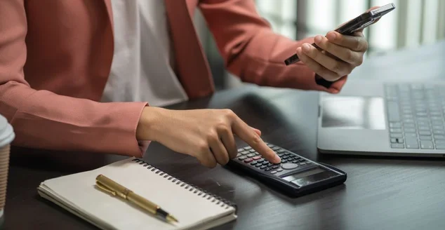 Close up de empresário trabalhando em calculadora para calcular relatório de dados financeiros, documento contábil e laptop no escritório, conceito de negócio.