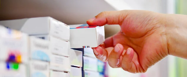 Mão segurando a caixa do medicamento na farmácia.