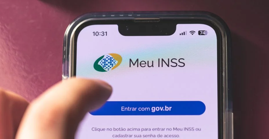 O aplicativo: Meu INSS, na tela de um smartphone. Instituto Nacional do Seguro Social. A mão de um homem na composição.