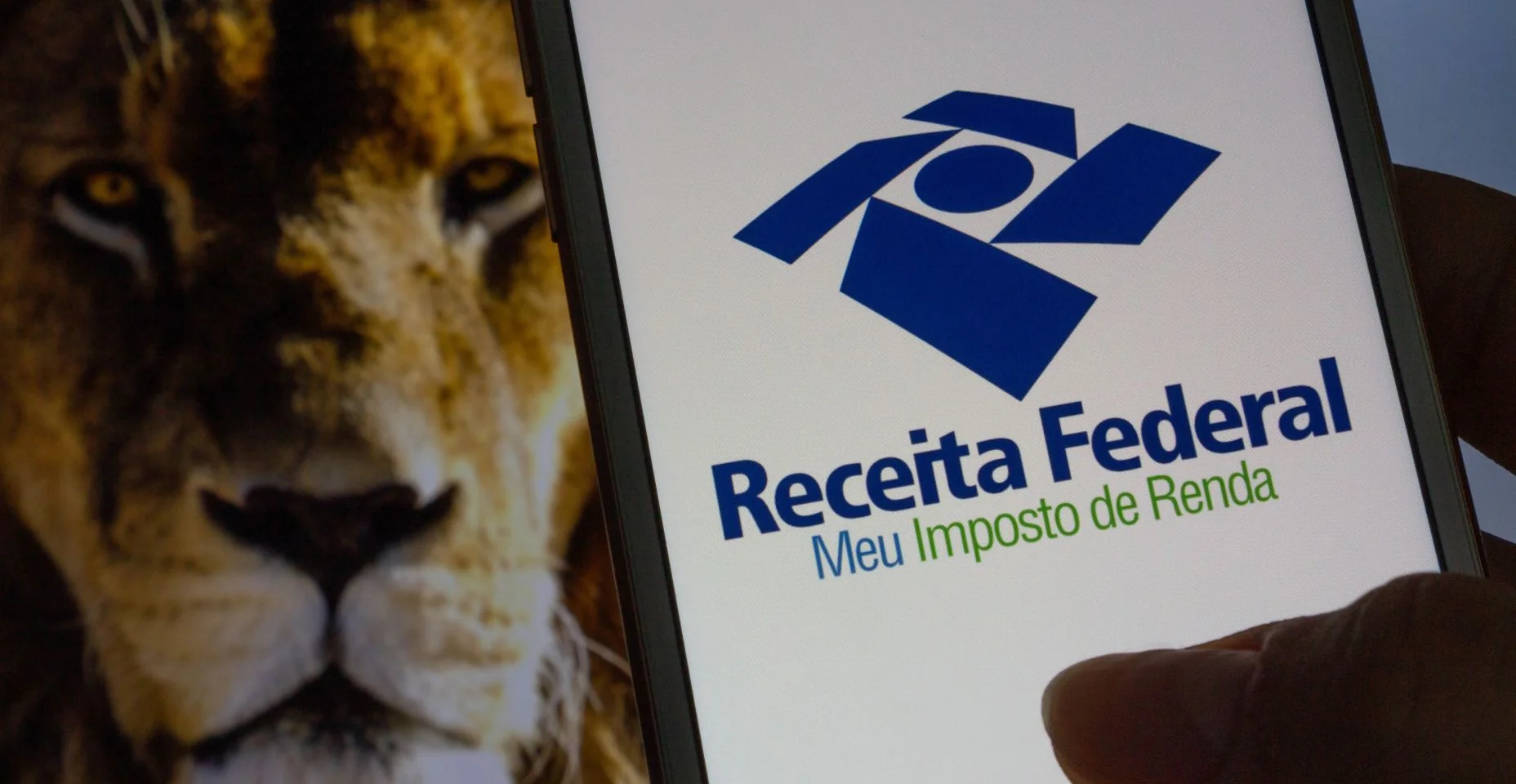 Aplicativo da Receita Federal (Receita Federal) - Mão segurando um celular branco com imagem de leão ao fundo. Foco seletivo