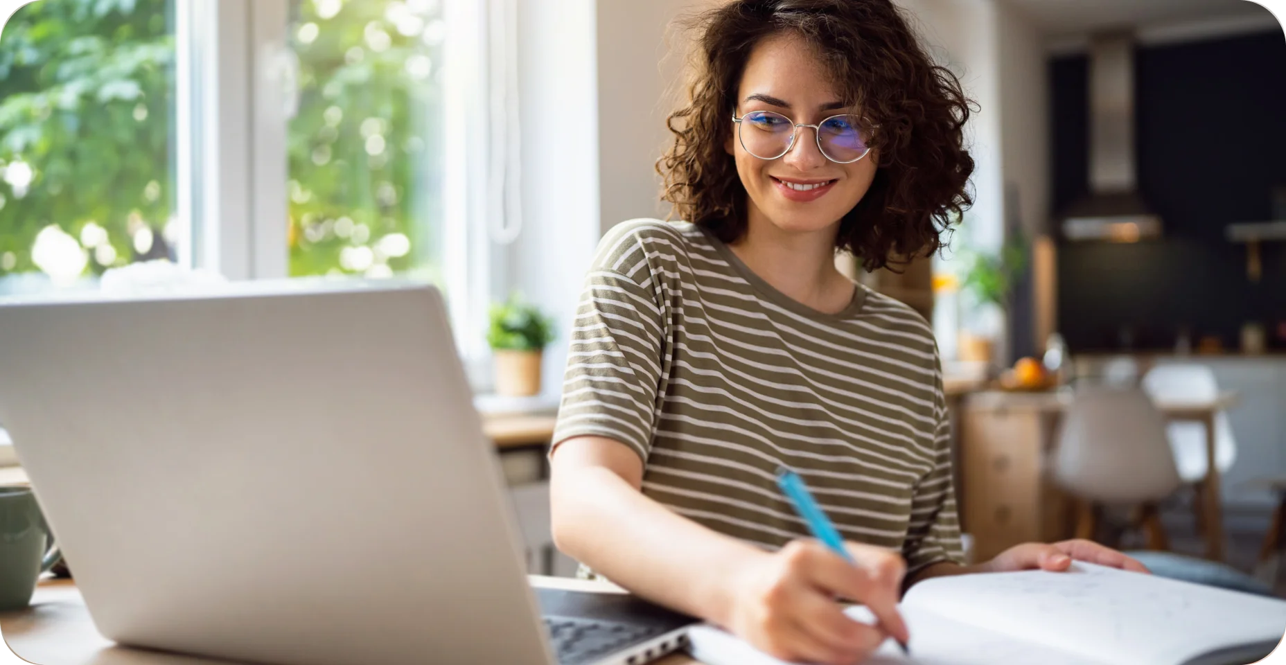 Mulher olhando para o computador e fazendo anotações em seu caderno