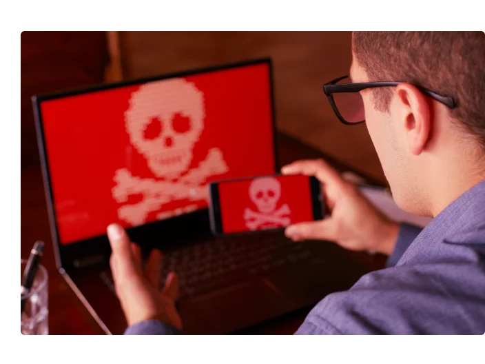 Homem senta-se perto de portátil com telefone bloqueado e criptografados pelo spyware ransomware pedindo dinheiro. Laptop e smartphone infectado pelo vírus. Caveira Vermelha assustador ossos na tela. Conceito de segurança cibernética