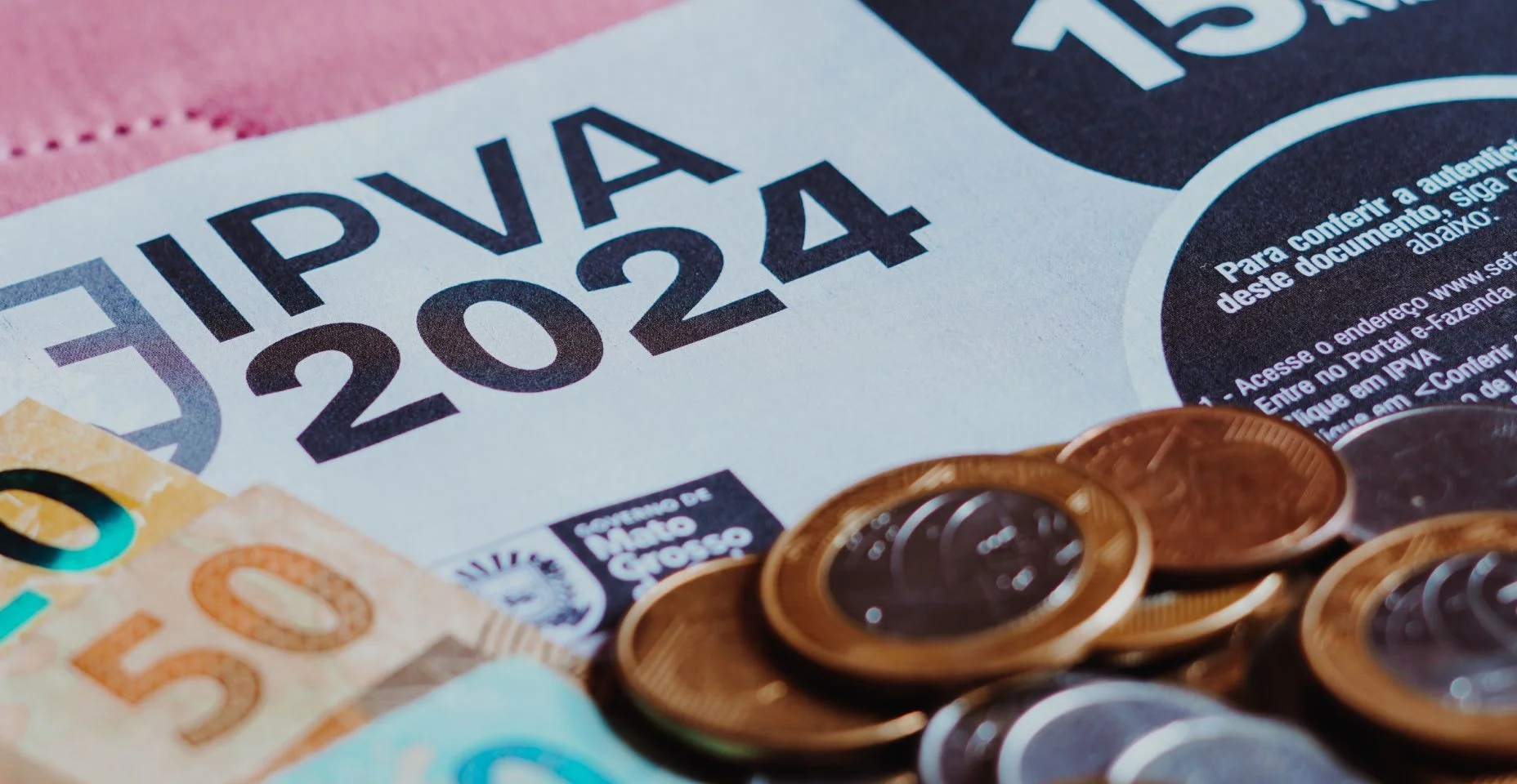 O boleto IPVA (Imposto sobre a Propriedade de Veículos Automotores) ao lado de cédulas e moedas de dinheiro real brasileiro.
