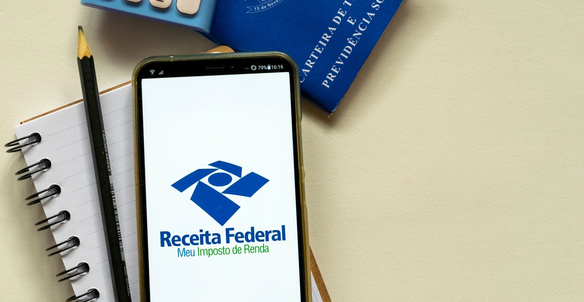 caderno, lápis, carteira de trabalho e um celular com o app da receita federal aberto