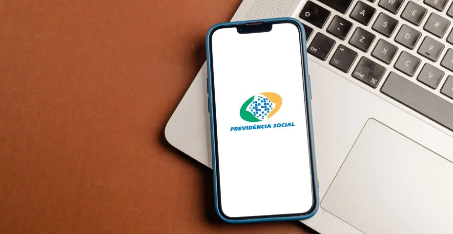 celular encostado no notebook com o logo do previdência social (inss) aberto