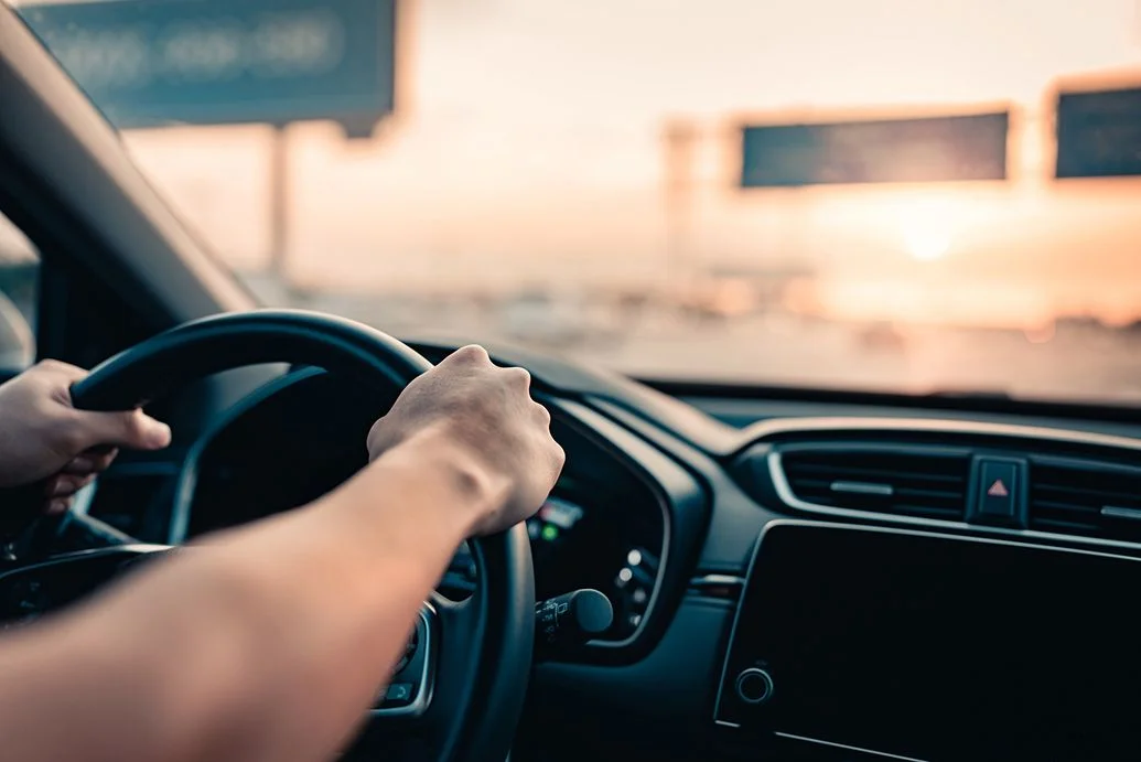Mão de homem dirigindo carro na estrada.
