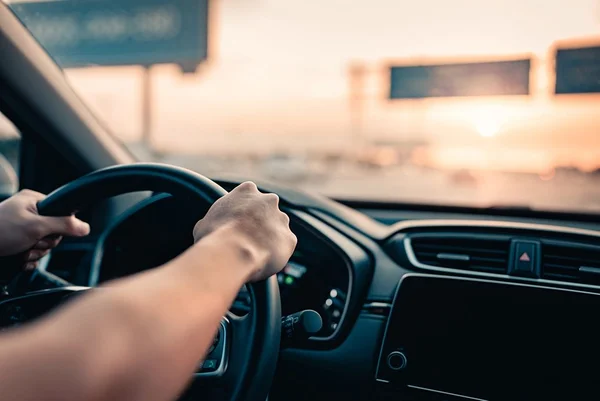 Mão de homem dirigindo carro na estrada.