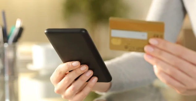 Mulher segurando telefone e cartão de crédito em uma mesa em casa