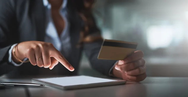 mulher de negócios segurando um cartão de crédito e apontando para um tablet que está na mesa