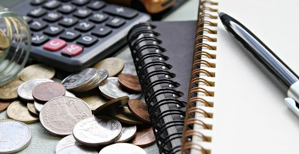 Modelo do carro em miniatura, calculadora, moedas espalhadas em frasco de vidro, papel de caderno e caneta na mesa de mesa de escritório