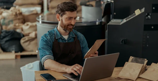 Dono de uma pequena fábrica de torrefação de café trabalhando laptop em seu local de trabalho