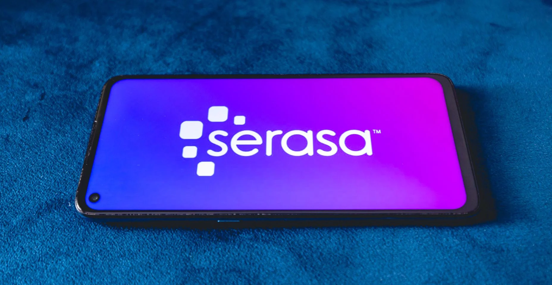 Um telefone celular com a logo da empresa brasileira Serasa sobre um sofá azul.