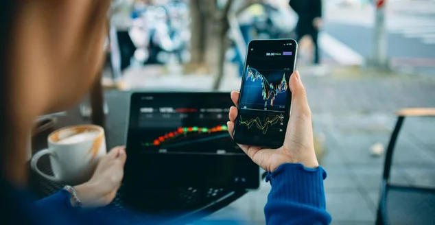 Mão de mulher de negócios usando telefone inteligente com loja de café. Gráficos do mercado de ações na tela do telefone e do laptop. Verificando o mercado financeiro.