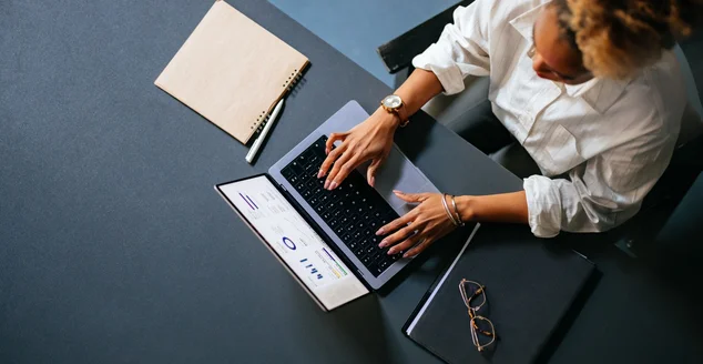 Visão de alto ângulo de mulher irreconhecível digitando relatório de negócios em um teclado de laptop no café