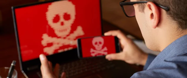 Homem senta-se perto de portátil com telefone bloqueado e criptografados pelo spyware ransomware pedindo dinheiro. Laptop e smartphone infectado pelo vírus. Caveira Vermelha assustador ossos na tela. Conceito de segurança cibernética