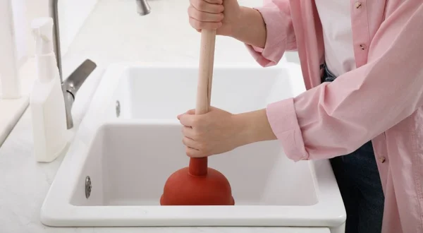 Mulher usando êmbolo para desentupir dreno de pia na cozinha, close-up