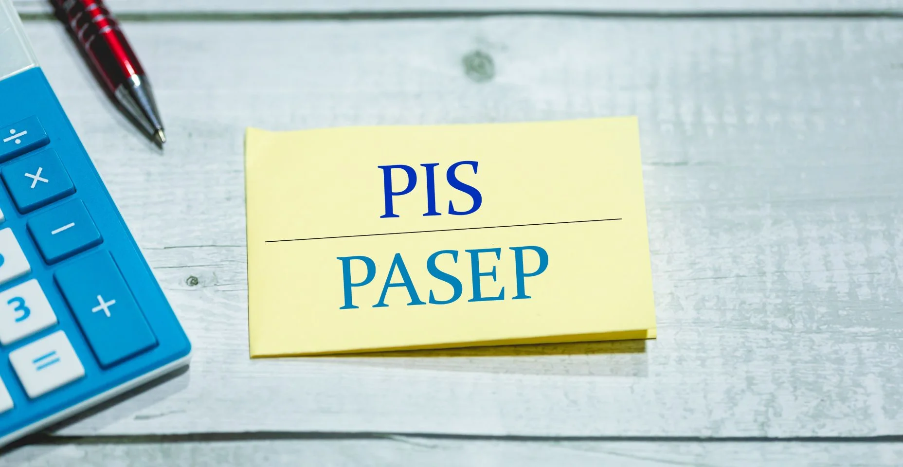 As siglas PIS e PASEP escritas em um pedaço de papel que está sobre uma mesa de madeira. Uma calculadora e uma caneta na composição. Economia brasileira.