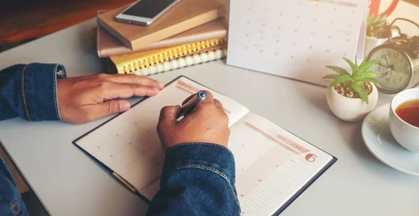 Mão masculina de planejador escrevendo agendamento diário no livro calendário 2020