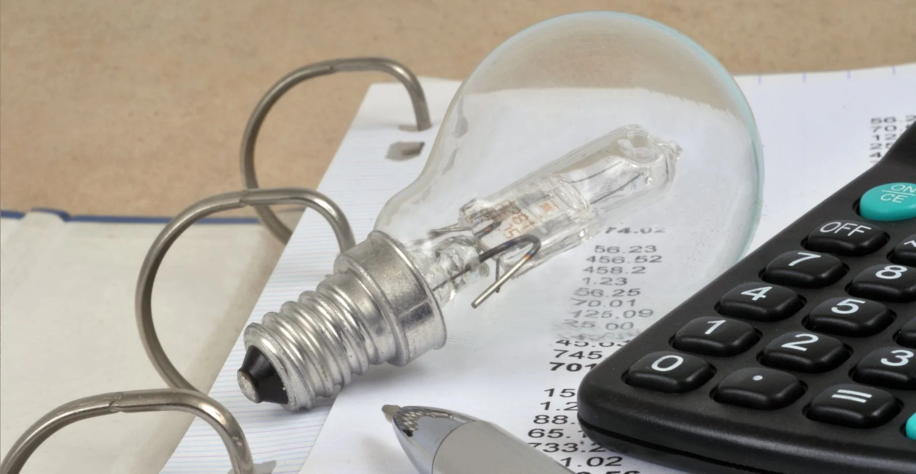 Lâmpada com moedas, notebook com uma caneta e calculadora e conta de luz em um fundo de madeira