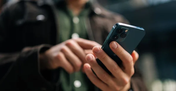 Mãos de close-up de homem irreconhecível segurando e usando smartphone em pé na rua da cidade, navegando na internet, verificando as mídias sociais, usando o aplicativo móvel
