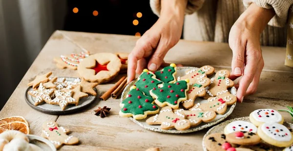 Mãos da mulher que arranjam doces na tabela do Natal