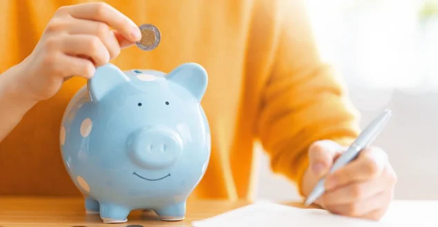 Mão colocando moeda em um cofre de porquinho azul