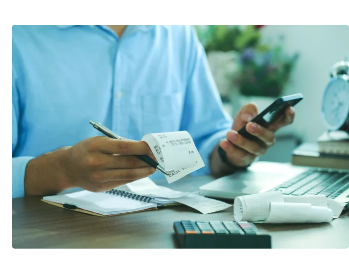 Homem segurando um notinha e um celular fazendo os calculos