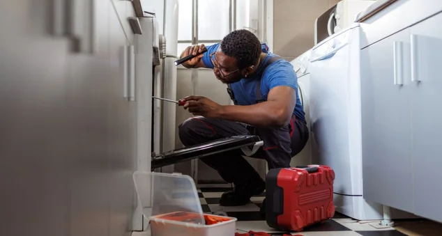Jovem consertando fogão na cozinha de um cliente