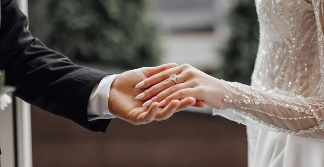 O homem segura gentilmente a mão da noiva com uma linda aliança de casamento dourada. Imagem ampliada das mãos dos recém-casados. Conceito de casamento. O noivo toca suavemente a noiva