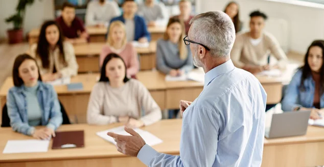 Visão traseira do professor maduro conversando com seu aluno durante palestra na sala de aula da universidade.