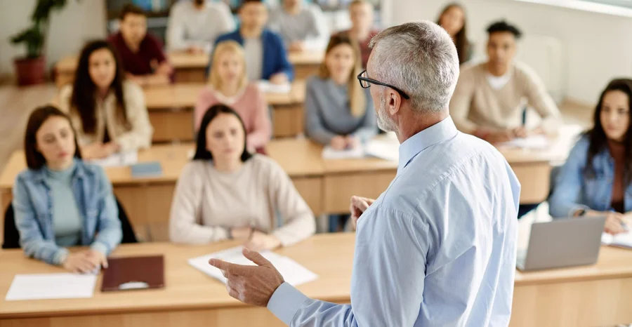Visão traseira do professor maduro conversando com seu aluno durante palestra na sala de aula da universidade.