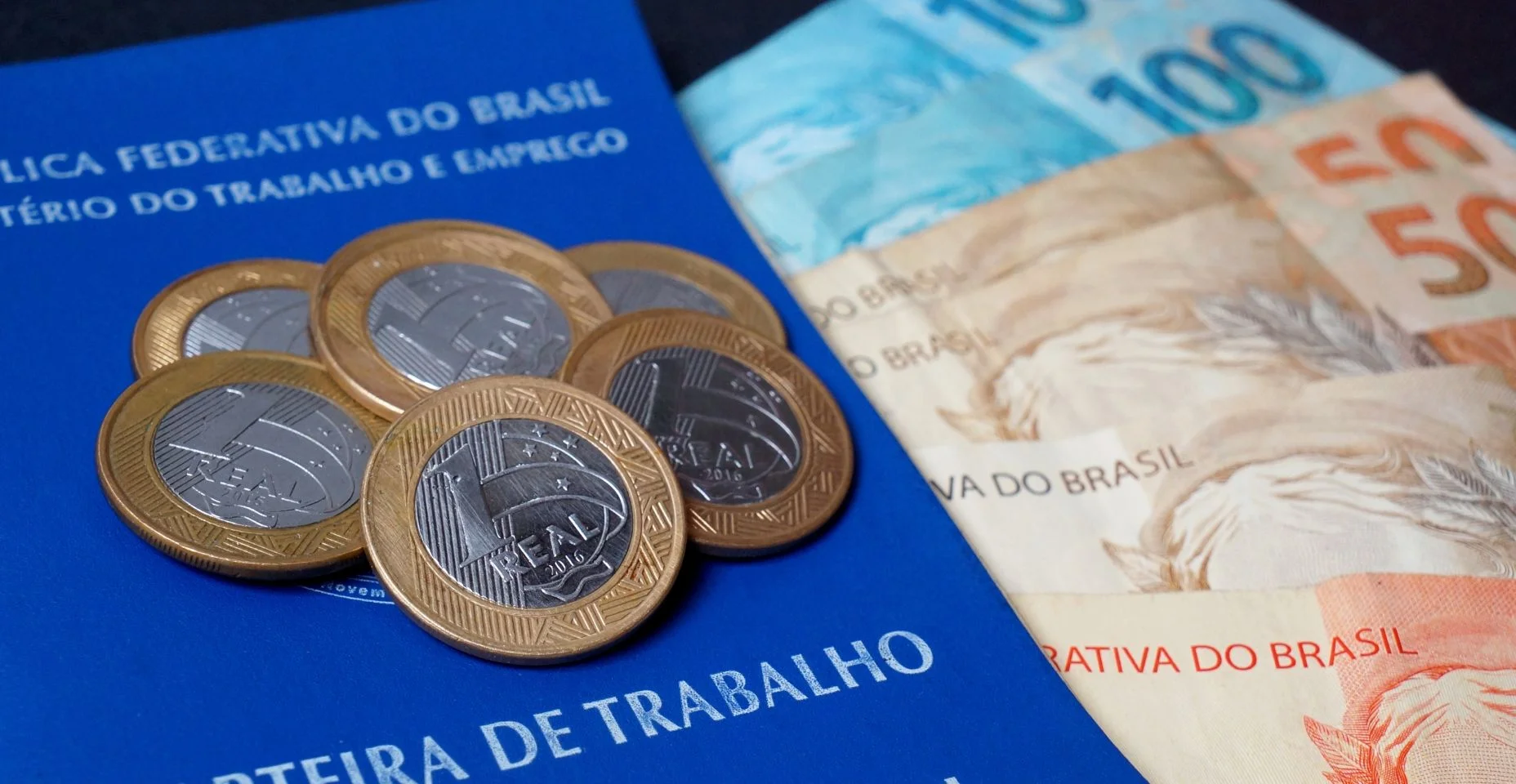 Carteira de trabalho brasileira com cédulas e moedas. Dinheiro brasileiro. Conceito de salário e emprego.