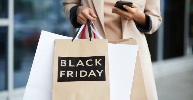 Retrato intermediário de uma jovem elegante segurando sacolas de compras na Black Friday e enviando mensagens de texto enquanto sai do shopping na temporada de vendas