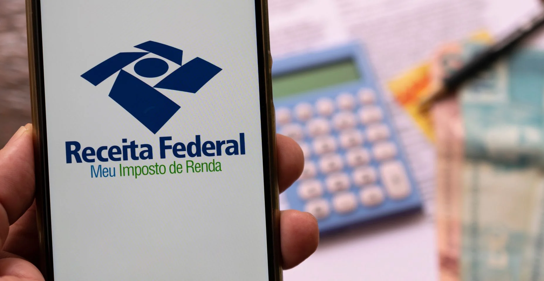 celular em mãos com requerimento da Receita Federal para declaração de imposto de renda. Foco seletivo.