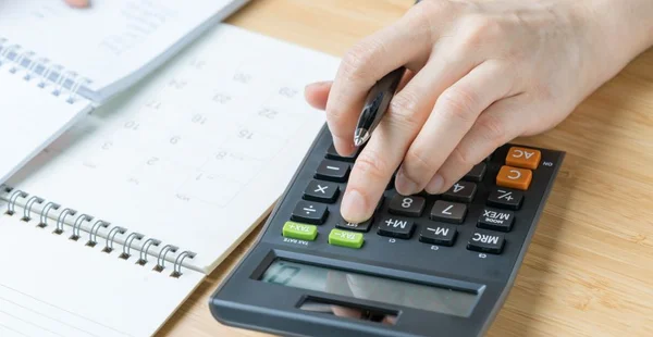 Despesa, conceito de cálculo de orçamento, feminino mão segurando a caneta, cálculo de custo com o bloco de notas e calendário de mesa de madeira