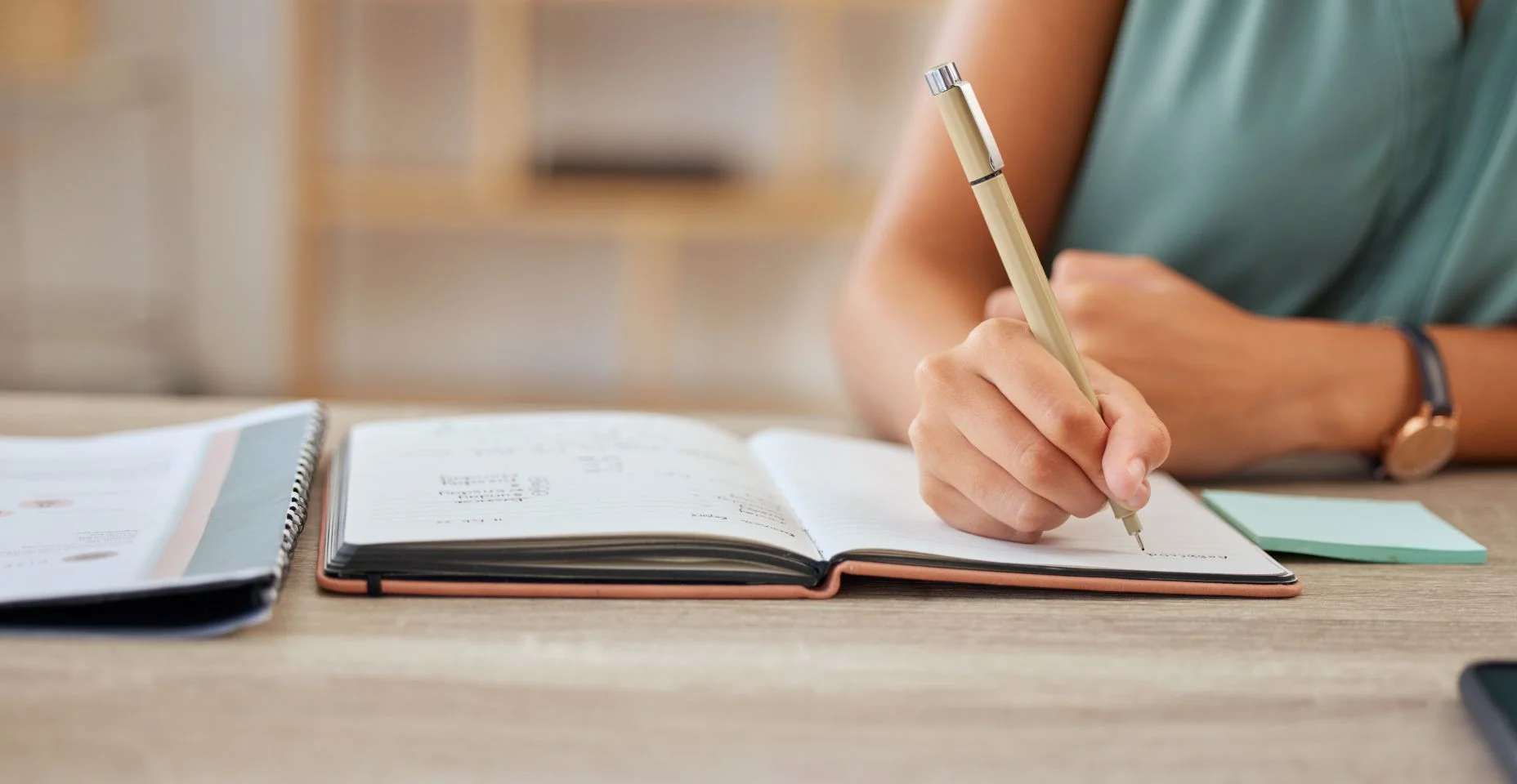 Mão, caneta e escrita em um caderno com uma mulher de negócios sentada em uma mesa em seu escritório para planejamento. Agenda, horário e compromisso com uma funcionária fazendo anotações em seu diário ou diário