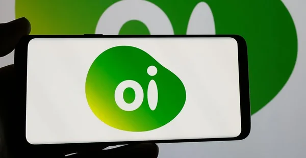 Pessoa segurando smartphone com o logotipo da empresa brasileira de telecomunicações Oi SA na tela. Foco na tela do telefone.