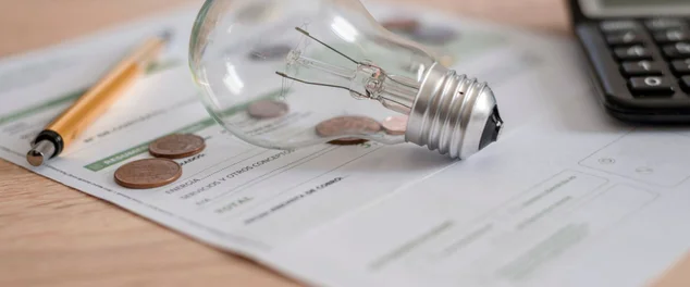 Conta de luz com lâmpada, várias moedas, calculadora e caneta na mesa. Conceito de preços de eletricidade e pagamentos de impostos.