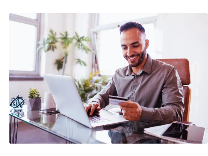 Meio adulto sorridente empresário latino no escritório, usando cartão de crédito para pagar online