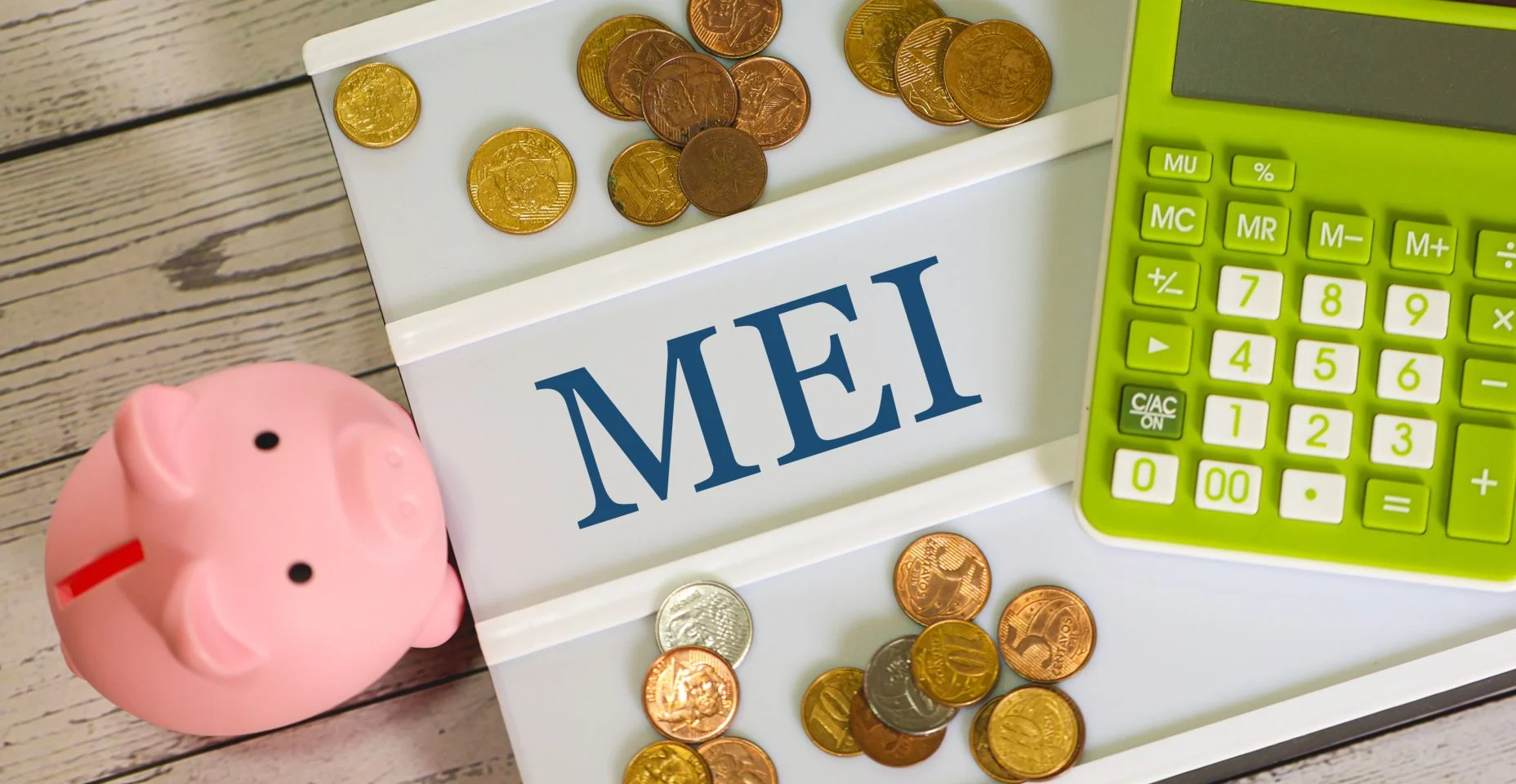 A sigla MEI para Microempreendedor Individual escrita em um quadro de cartas com uma calculadora, um cofrinho e moedas de reais na composição. Economia brasileira.
