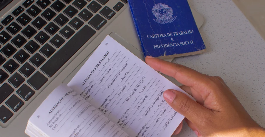 República Federativa do Brasil, Ministério do Trabalho. Carteira de trabalho brasileira em frente a um laptop, ilustrando a relação entre documentação legal e mercado de trabalho