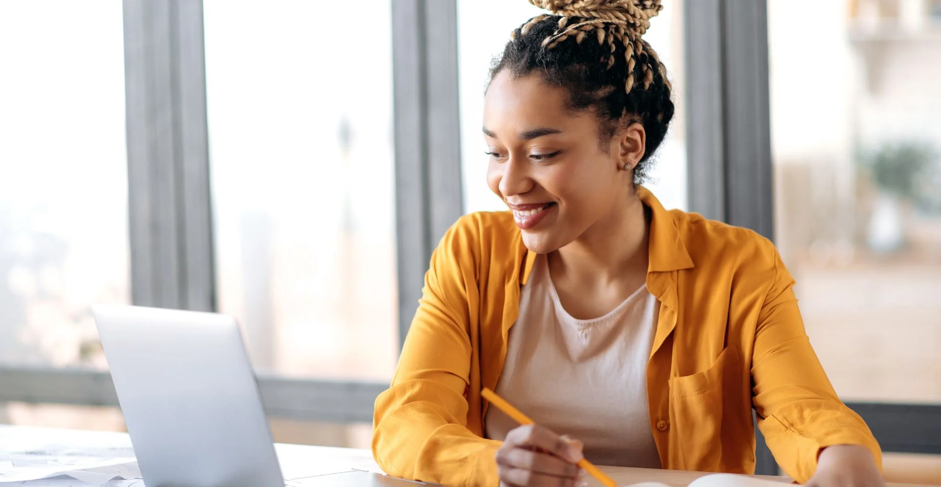 Educação online, e-learning. Feliz jovem afro-americana em roupas casuais elegantes, estudando remotamente, usando um laptop, ouvindo palestras online, tomando notas enquanto estava sentada em casa, sorri