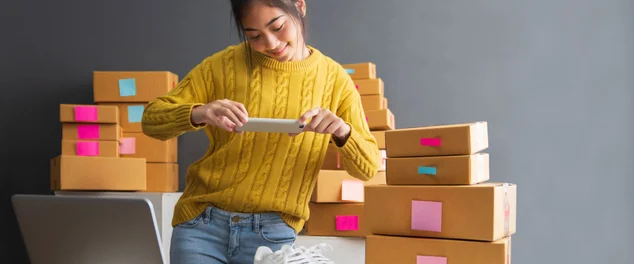 Mulheres novas que tomam a foto às sapatas com telefone de pilha ou câmera digital do smartphone para o borne para vender em linha no Internet e em preparar a caixa do produto do bloco. Vendendo o conceito em linha das idéias