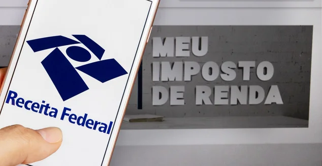 Aplicativo da Receita Federal (Receita Federal) - Mão segurando um celular branco com "meu imposto de renda" ao fundo. Foco seletivo.