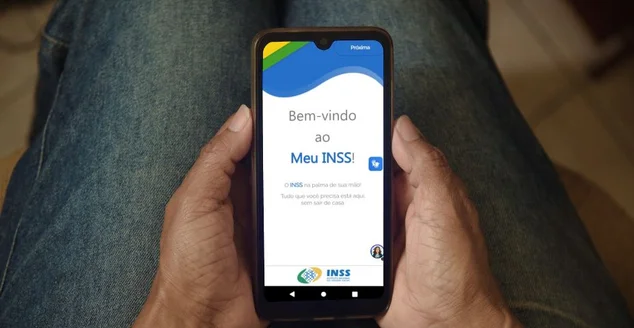 Instituto Nacional do Seguro Social. Aplicativo Meu INSS na tela de um celular que uma mulher segura.