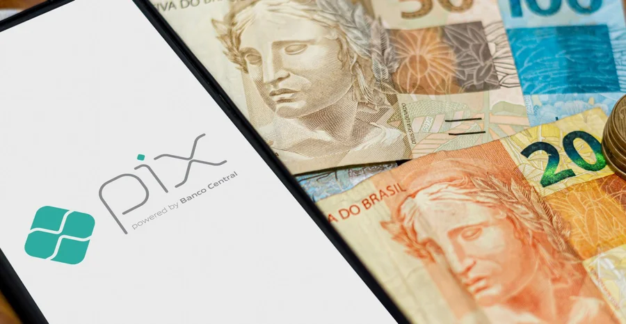 Logotipo Pix na tela do smartphone com diversas moedas ao redor. Pix é o novo sistema de pagamentos e transferências do governo brasileiro e brasileiro.
